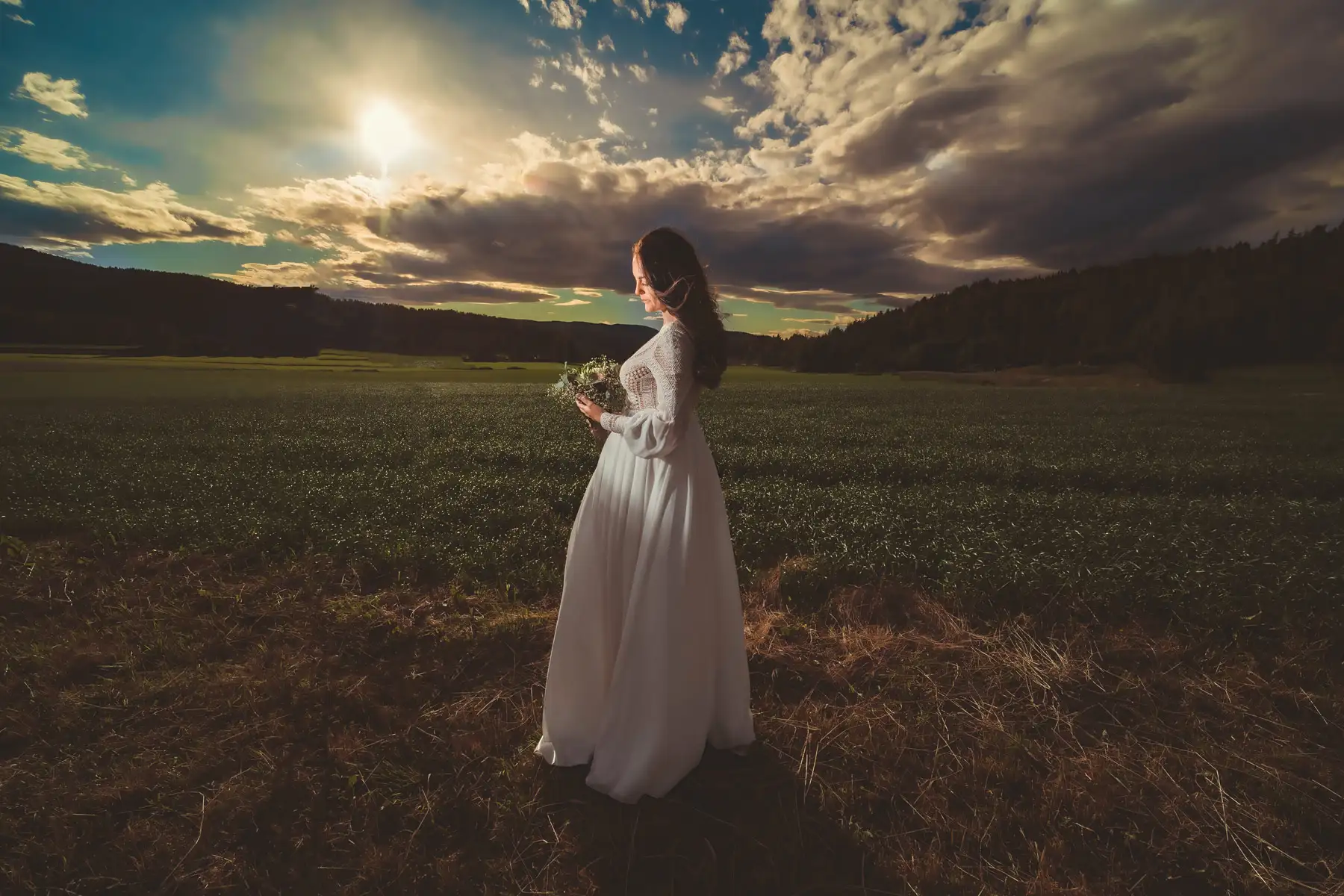 Bryllupsfotograf Oslo – brud i solnedgang med blomsterbukett og mykt landskap