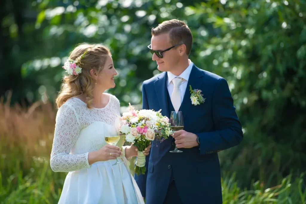 Bryllupsfotograf – stemningsfullt bilde av brudepar med vinglass i hage, tatt på Nedre Foss Gård, dokumentarisk stil med varme og naturlig grønn bakgrunn